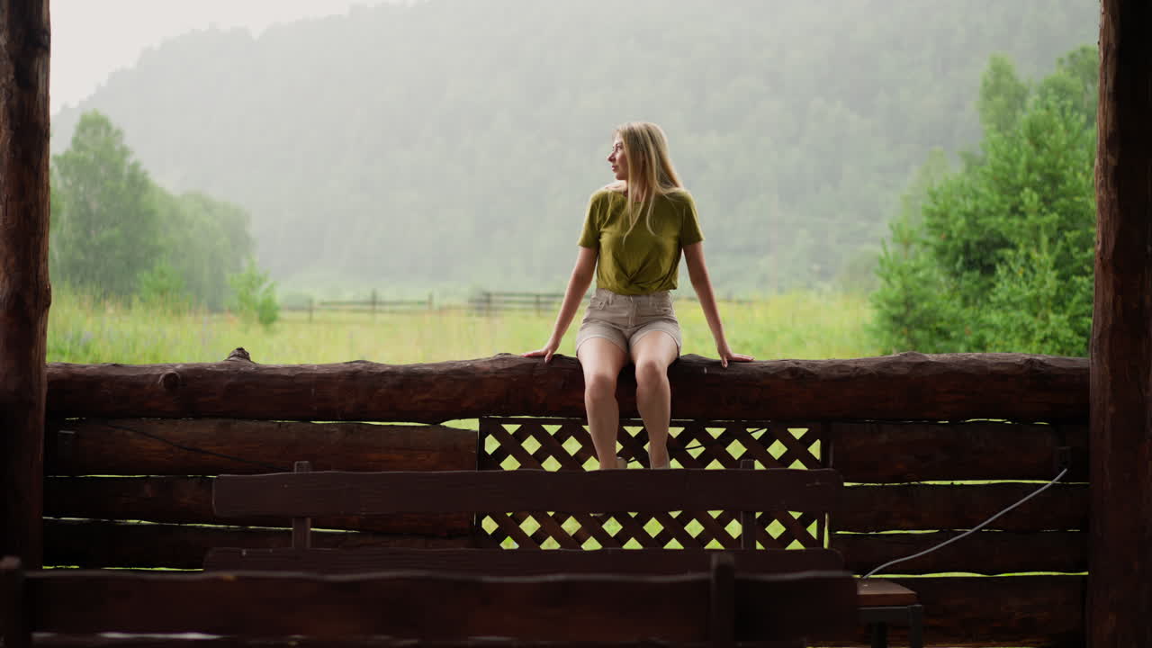 우아 한 여자 는 비 오는 날 에 나무 울타리 에 앉아 있는 것 을  ⁇  으로 본다