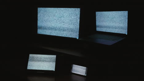 a side angle shot of four digital computer device screens displaying a choppy static noise pattern in a dark room