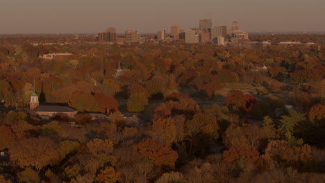 aerial push towards a small church, park, and city skyline in autumn
