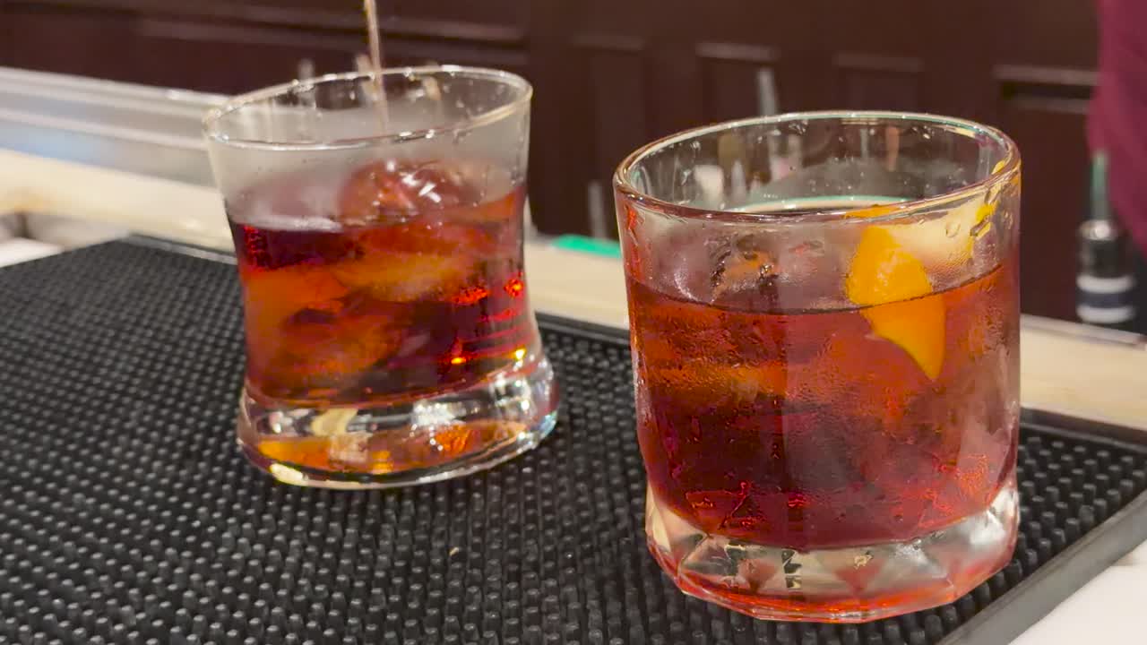 Un barista mescola un cocktail Negroni in un bicchiere con ghiaccio e guarnizioni, e lo serve in un bar elegante