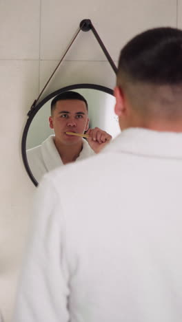 los amantes se cepillan los dientes frente a los espejos redondos colgantes en el baño. una pareja con túnicas de baño de terry lleva a cabo la rutina de cuidado nocturno de pie juntos. rutinaria higiénica