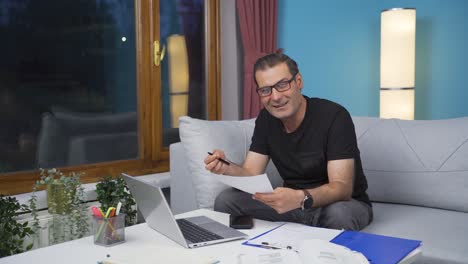 Home-office-worker-man-smiling-at-camera-looking-at-paperwork.