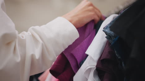 primer plano de la mano femenina seleccionando tela púrpura de un estante de ropa en una tienda minorista, mostrando una experiencia de compra reflexiva, colores vibrantes y atención a los detalles en un entorno de moda moderno
