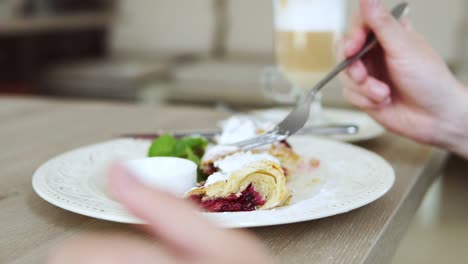 unrecognizable man in white t-shirt taking desert strudel at the restaurant using fork and knife and putting ice cream on