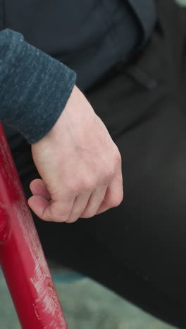 close-up of a person sitting on workout equipment, hands resting on the red bars while he shake his leg