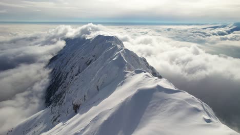 Montañas-Nevadas-De-Piatra-Craiului-Que-Alcanzan-Su-Punto-Máximo-A-Través-De-Un-Mar-De-Nubes-Bajo-Un-Cielo-Azul,-Vista-Aérea