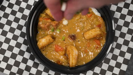 Hand-sprinkles-chopped-green-onions-over-bowl-of-crawfish-etouffee-with-shrimp,-slow-motion-overhead-4K