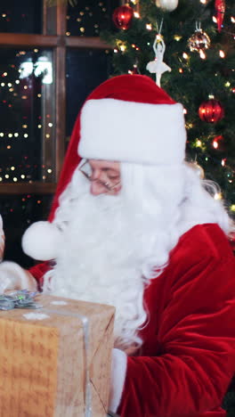 santa claus and elves in the evening in the room with new year's decorations prepare parcels with gifts for children. vertical video