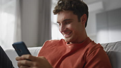 happy brunette texting cellphone sitting sofa closeup. joyful man typing sms