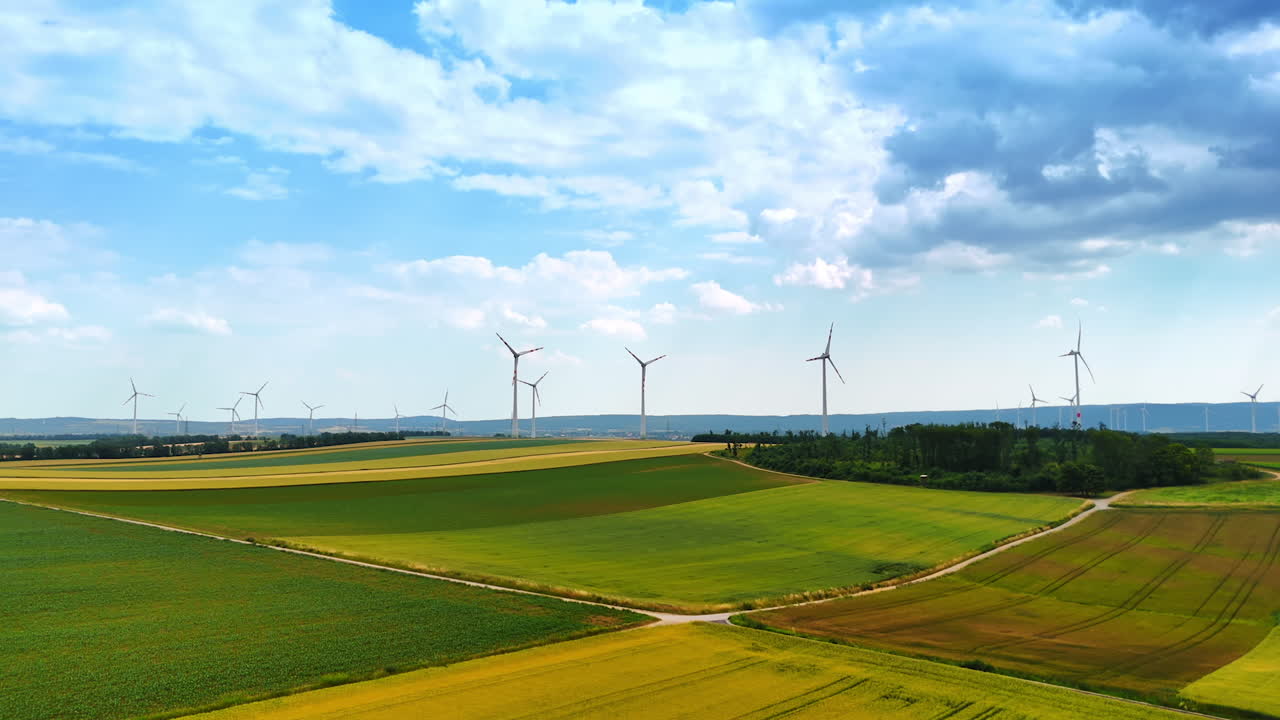 Green fields and blue cloudy sky with rotating wind mills. Green energy concept