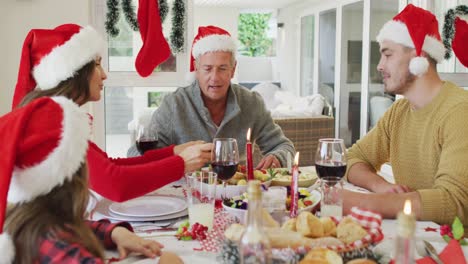 Feliz-Familia-Caucásica-Multigeneración-Con-Gorros-De-Papá-Noel,-Comiendo-Navidad