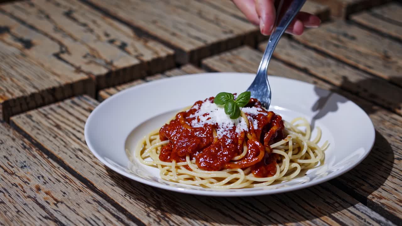 Video ravvicinato di una mano che arrotola spaghetti al pomodoro su una forchetta, su un tavolo rustico in legno