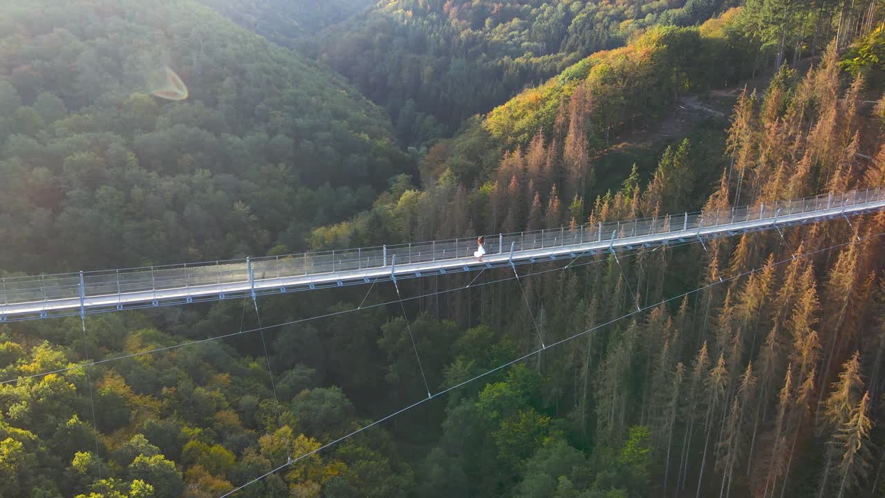 Aerial shot of young woman running across Geierlay suspension bridge in Western Germany