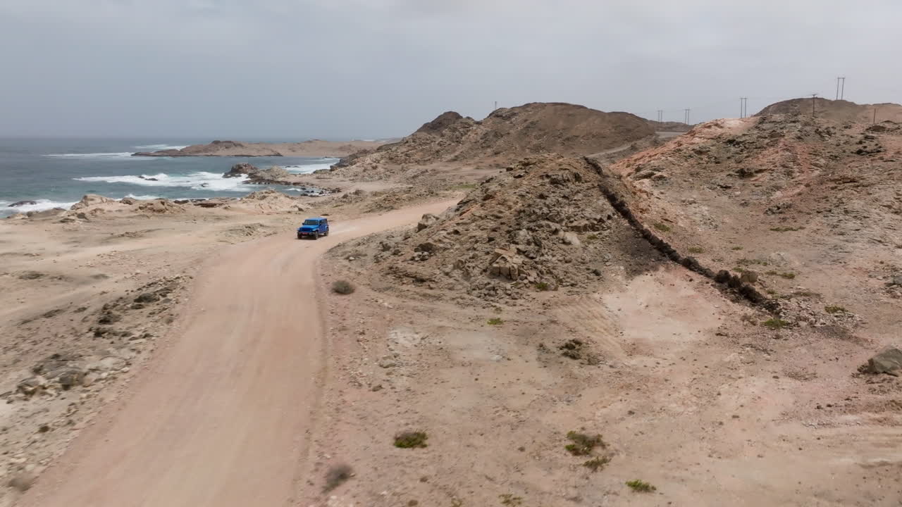 Desert road near the coast in Oman with a blue car driving along it