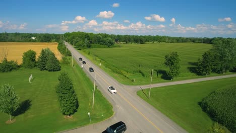 Black-cars-driving-down-a-country-road-on-a-clear-day,-pulling-up-to-a-venue