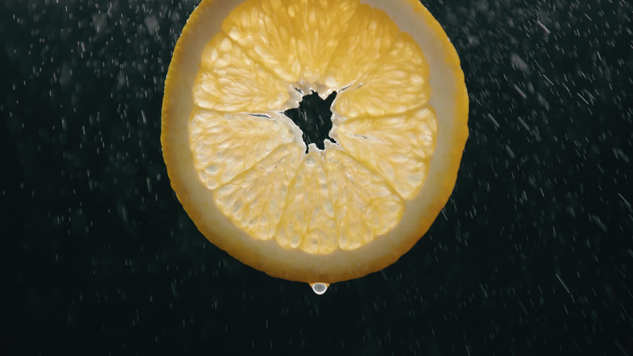 Fresh Orange Slice Splashed by Water Droplet Mist with Liquid Drip in Slow Motion Backlit Black Background