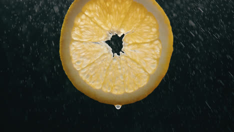rodaja de naranja fresca salpicada por niebla de gotas de agua con goteo líquido en cámara lenta con fondo negro retroiluminado