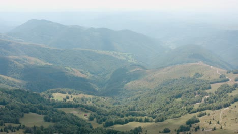 Vista-Aérea-Del-Pintoresco-Valle-Brumoso-Bajo-Las-Colinas-Montañosas-En-El-Campo-De-Serbia-En-La-Temporada-De-Verano,-Disparo-De-Drones