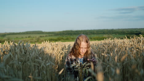 a teenage girl with long hair and a bouquet of spikelets of wheat sits in a wheat field. summer on the farm