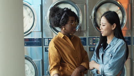 Mixed-Races-Stylish-Young-Girls-Best-Friends-Talking-And-Sharing-Secrets-While-Standing-In-Laundry-Service