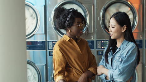 mixed races stylish young girls best friends talking and sharing secrets while standing in laundry service