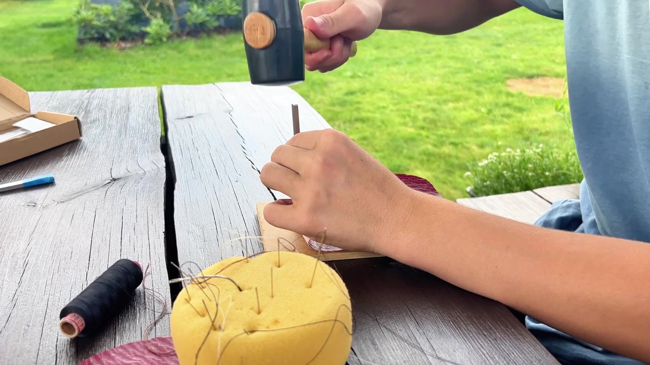 Primo piano di mani che cuciono pelle all'aperto usando strumenti specializzati. Perfetto per tutorial fai da te, laboratori artigianali, branding artigianale e contenuti per hobby.