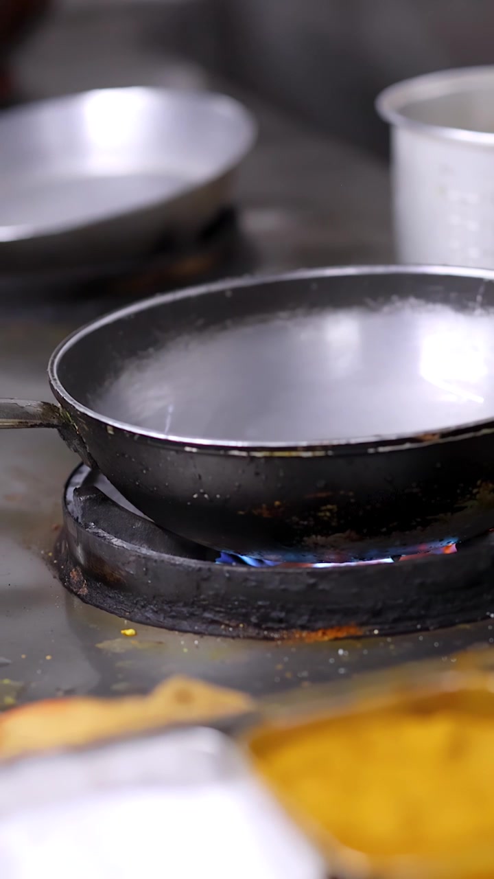 Static close-up shot of empty frying pan heating over blue gas flames in professional kitchen.