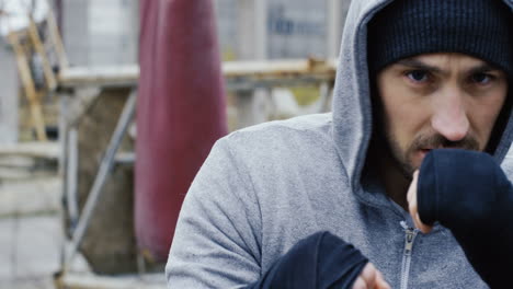 close-up view of handsome bearded caucasian man wearing grey hoodie and boxing to the camera outdoors an abandoned factory on a cloudy morning