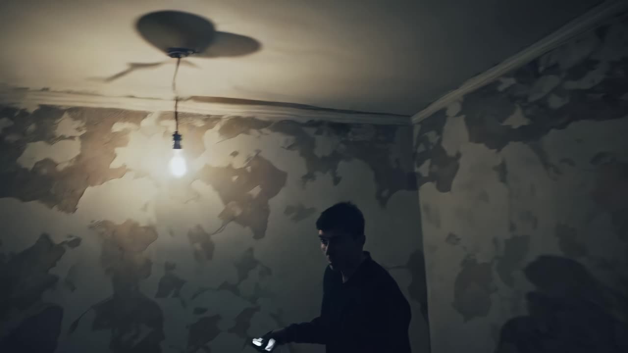 Moody video scene with a dimly lit room, peeling wallpaper, and a single bulb