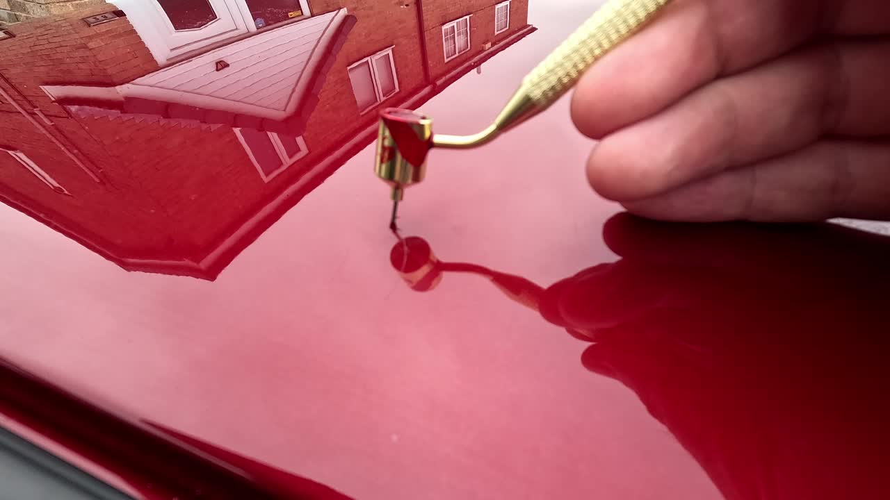 Touching in a scratch on a red car with fine touch up pen applicator - close up