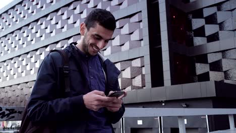 young happy middle eastern man using a smartphone and smiling in city