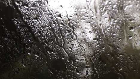 raining on a cars window with the rain drops flowing down, forest in the background