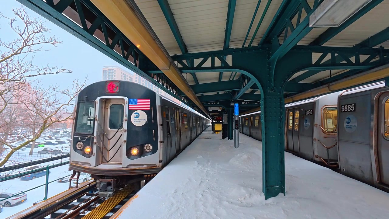 New York, USA, 25 dicembre 2025: Stazione della metropolitana sopraelevata in inverno, New York City. Il treno F si avvicina a una banchina dove la neve copre i binari, le ringhiere e le aree pedonali.