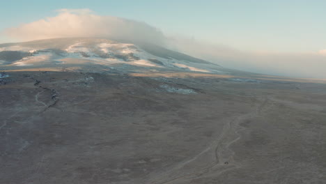 Aerial-orbits-vehicle-parked-at-base-of-large-mountain-in-desert-wilderness