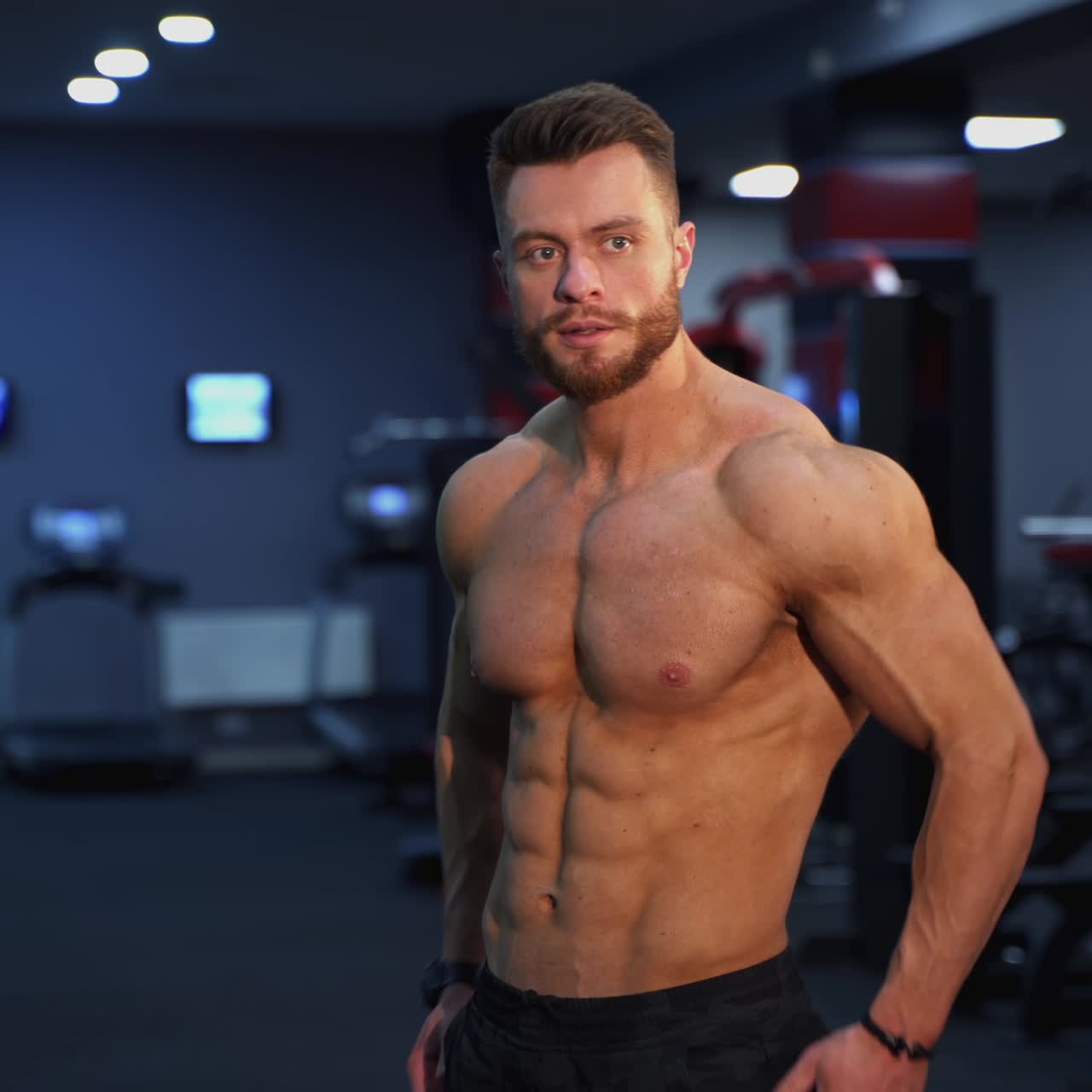 Portrait muscular male bodybuilder with naked body. Handsome sportsman posing on camera in the gym. Confident strong fitness trainer after training in a sports club