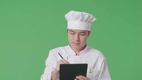 el chef asiático tomando nota en una tableta mientras camina en el estudio de fondo de la pantalla verde