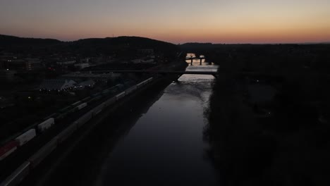 an aerial view of the lehigh river in bethlehem, pennsylvania, after sunset with long cargo trains on the left of the shot