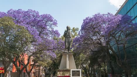 Tiro-De-ángulo-Bajo-De-Hiperlapso-De-Estatua-Tradicional,-Flores-Alrededor-En-Un-Día-Soleado,-Ciudad-De-México