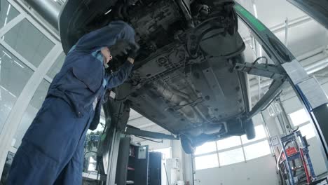 mecánico de automóviles que trabaja debajo de la máquina de elevación de automóviles en el garaje. taller de reparación de autos, servicio de automóviles, reparación.