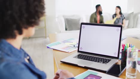 Mujer-Birracial-Haciendo-Videollamadas-Con-Laptop,-Copiando-Espacio-En-Pantalla,-Colegas-Detrás,-Cámara-Lenta