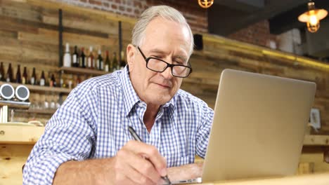 Senior man writing down while using laptop 4k