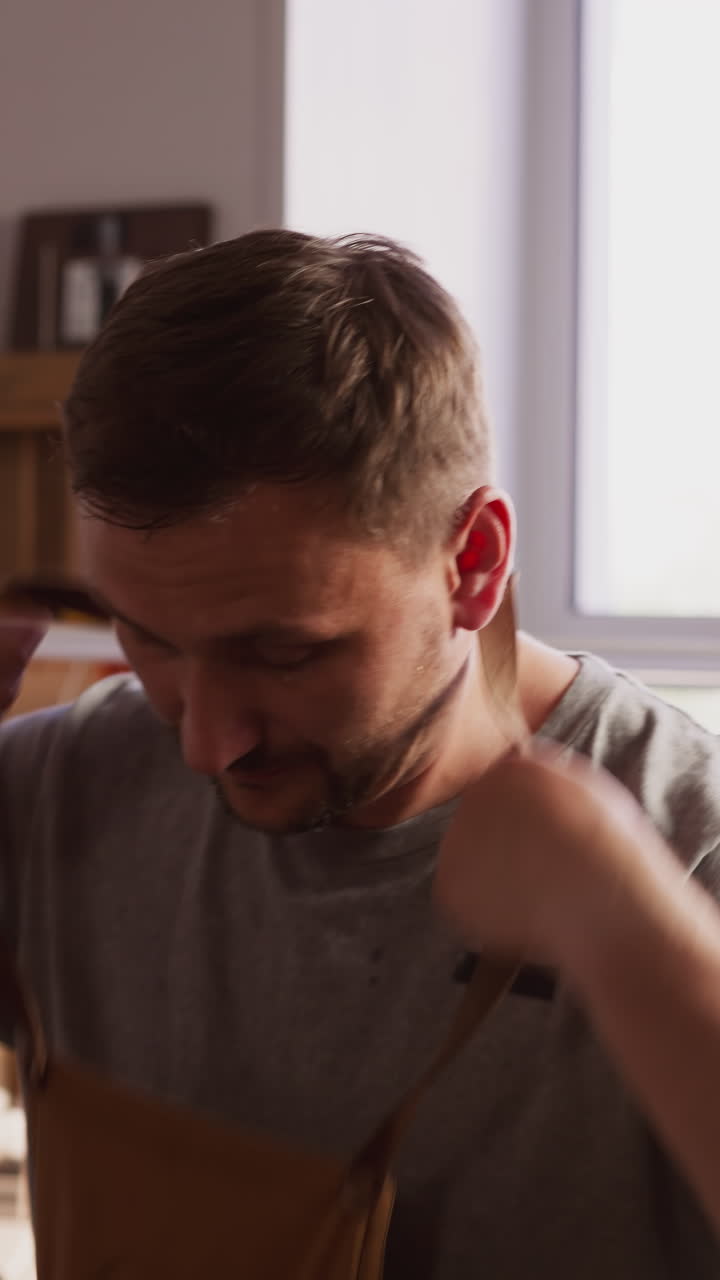 Male employee puts on protective apron ready for work in craft studio slow motion. Leathersmith with workwear in shop. Skilled craftsman at workplace