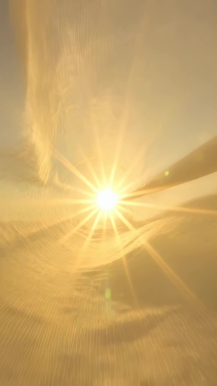 Vertical video: Spinning propeller crossing low sun over cloud deck, casting shadows and lens flare