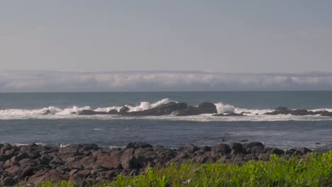 A-landscape-shot-of-waves-crashing-onto-rocks-just-off-a-grassy-shore