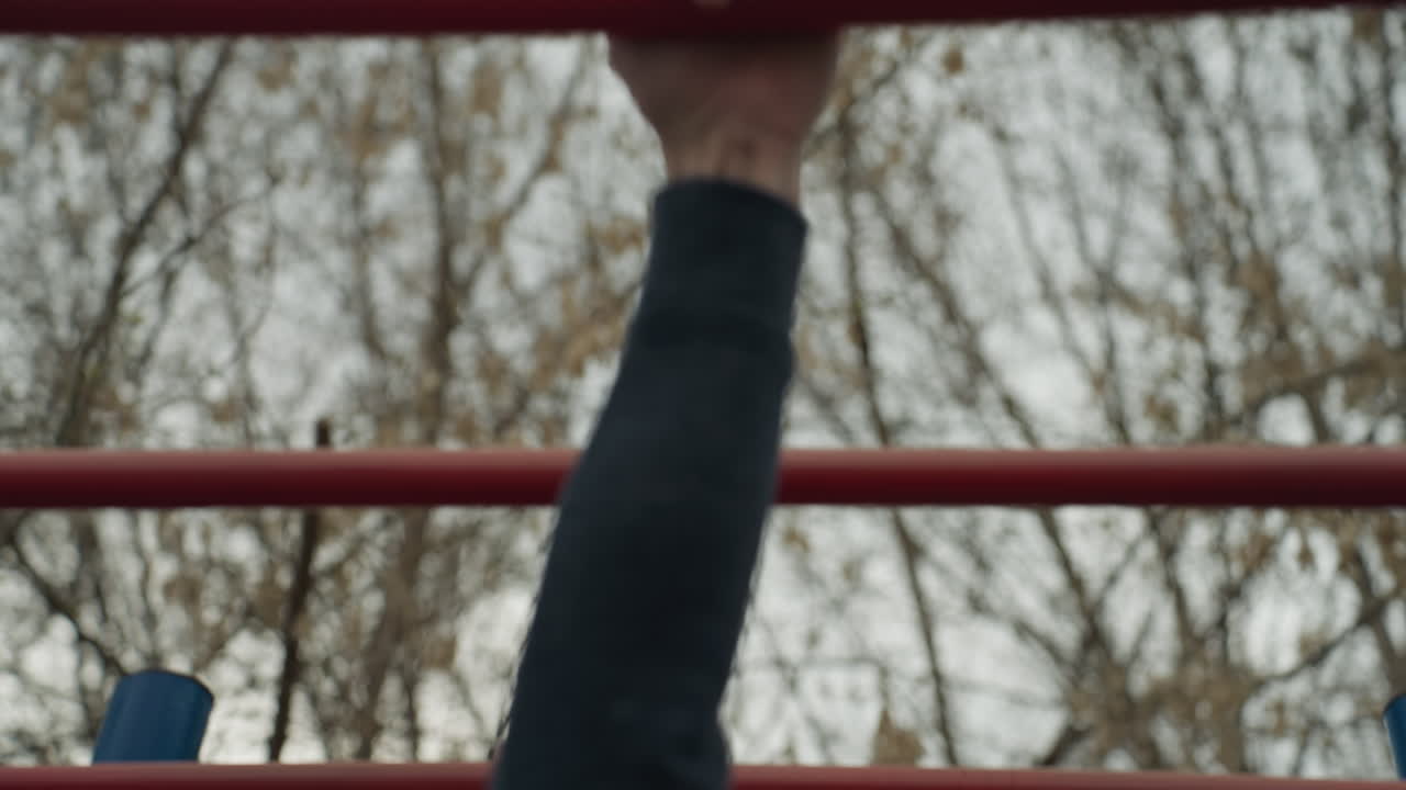 close up of a someone's hand holding a red iron bar as he moves over to the other iron bar, with bare tree seen above