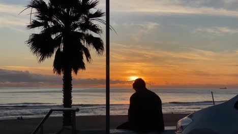 Hombre-De-Silueta-Sentado-En-Un-Banco-Al-Atardecer,-Luego-Se-Aleja,-En-Cámara-Lenta