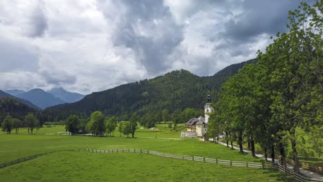 timelapse of storm clouds above small alpine village and church surrounded by meadows and tree alley, zgornje jezersko, slovenia