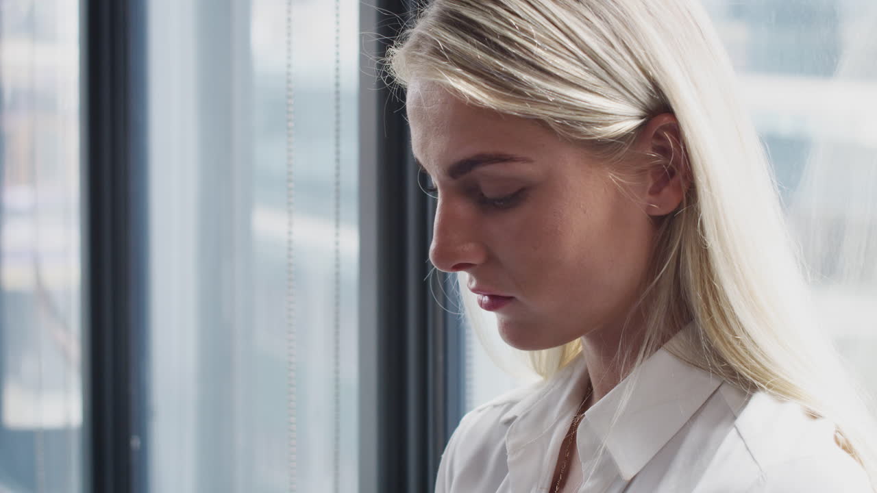Millennial, blonde weiße Frau benutzt einen Computer in einem Büro, Seitenansicht, Brustbild.