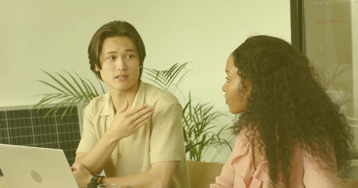 男同事俯身向前，比劃著手勢，展開商務洽談，同時圖表在手提電腦周圍增長。