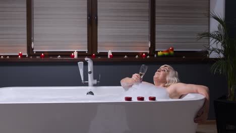 anciana anciana acostada en un baño caliente con burbujas, disfrutando de la relajación, bebiendo champán